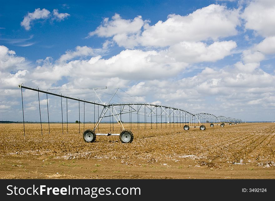 A mechanical sprinkler irrigation system stationed in a large uncultivated field.