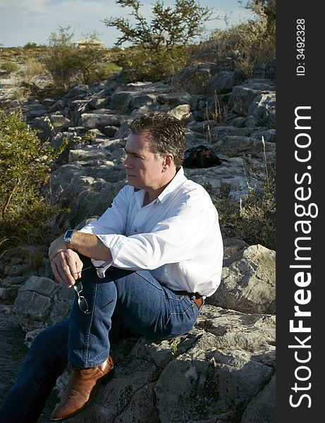 A man, leisurely enjoying the view from his perch on the side of a rocky hill. A man, leisurely enjoying the view from his perch on the side of a rocky hill.