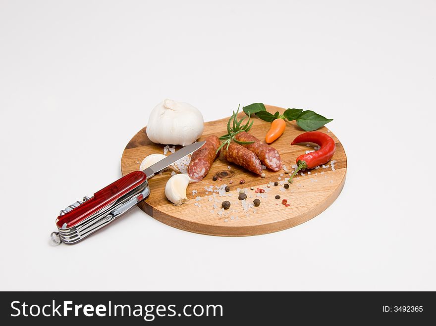 Various spices and sausages on a wooden plate and a swiss knife. Various spices and sausages on a wooden plate and a swiss knife