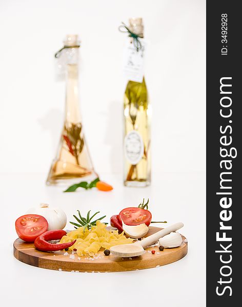 A wooden plate with tomatoes, pasta, garlic and spices in front of a vinegar- and oilbottle. A wooden plate with tomatoes, pasta, garlic and spices in front of a vinegar- and oilbottle