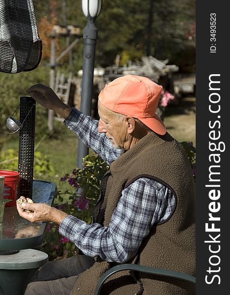 Senior man putting peanuts  for the birds into a manger. Senior man putting peanuts  for the birds into a manger