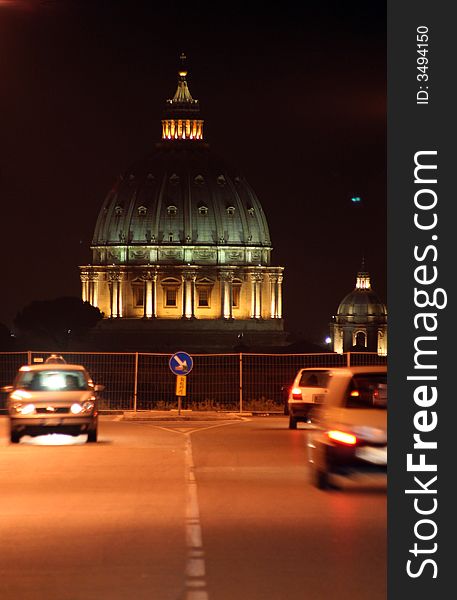 St. Peter's (Rome - Italy - Vatican City) Basilica at night / Evocative lights on the Dome / View from a urban road with vehicles movement / Signal road with arrow right. St. Peter's (Rome - Italy - Vatican City) Basilica at night / Evocative lights on the Dome / View from a urban road with vehicles movement / Signal road with arrow right