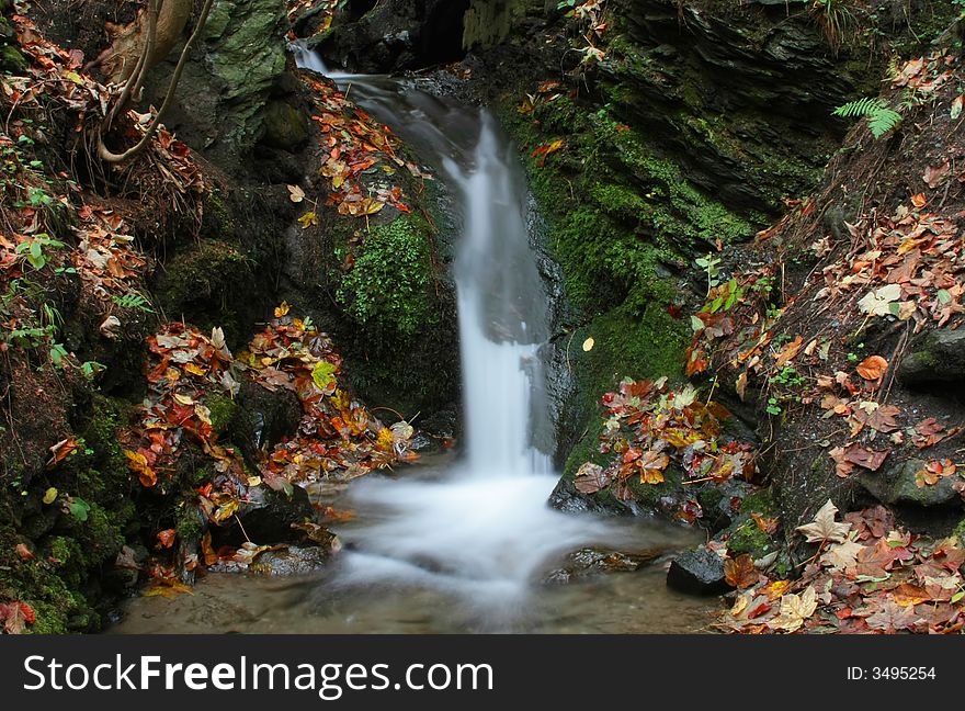 Small waterfall surrounded by autumn colored leaves and green moss. Small waterfall surrounded by autumn colored leaves and green moss