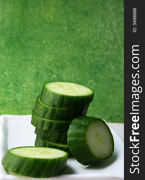 Sliced cucumber on white plate with green background