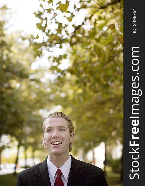 One businessman looking past camera with open mouth dressed in business full suit with red tie and trees in background. One businessman looking past camera with open mouth dressed in business full suit with red tie and trees in background