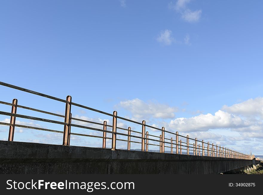 A bridge crosses the lagoon and marshes to reach the sea. in the background blue sky with clouds. A bridge crosses the lagoon and marshes to reach the sea. in the background blue sky with clouds.