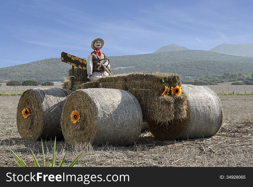 Cute scarecrow built atop a tractor with straw.