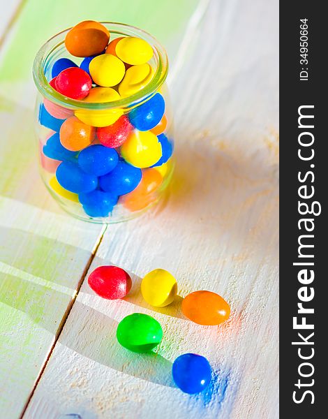 Colored candy in glass jar on wooden background