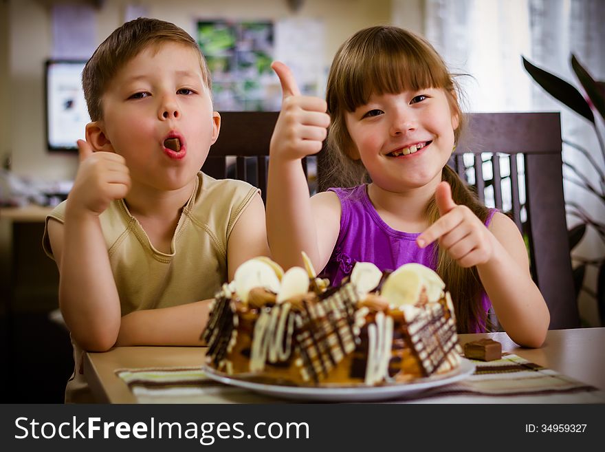 Children sit near a table and eat a cake. Children sit near a table and eat a cake