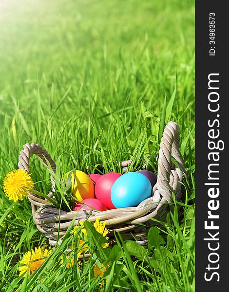 Wicker basket with Easter eggs and flowers in the grass