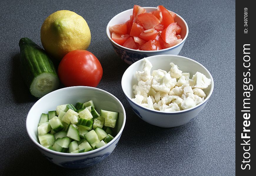 Tomato, cauliflower, and cucumber in three blue bowls on blue background. There is a whole tomato, cucumber, and lemon in the picture too. Tomato, cauliflower, and cucumber in three blue bowls on blue background. There is a whole tomato, cucumber, and lemon in the picture too.