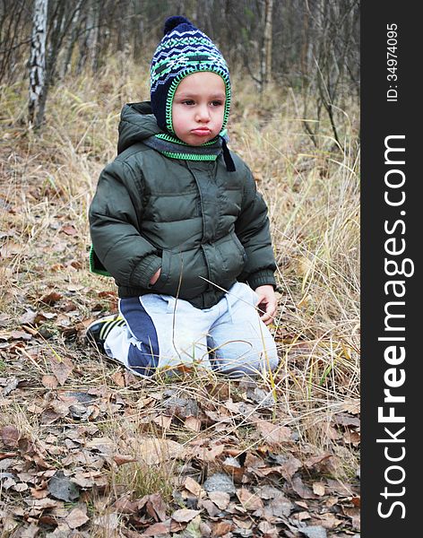 In the autumn forest sitting on the grass sad upset boy