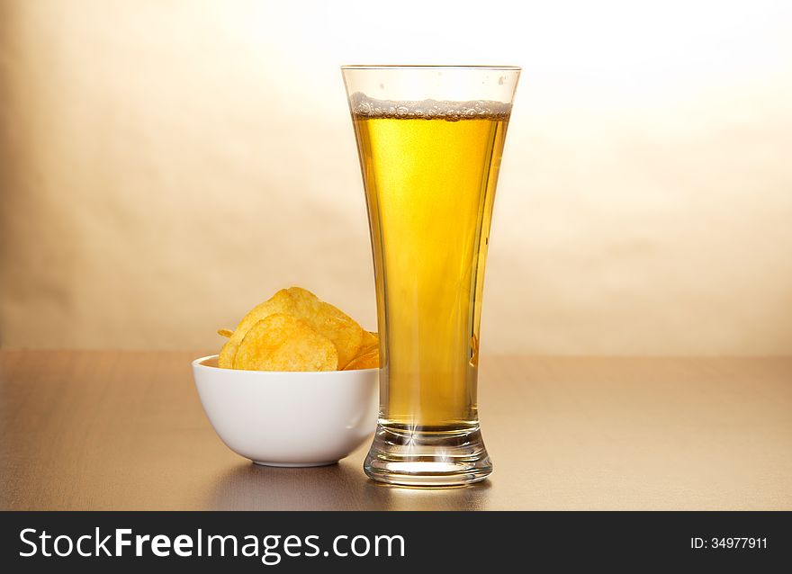 Glass of light beer and bowl with chips against paper