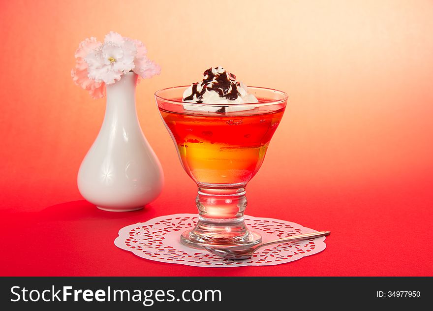 Glass with a dessert, a teaspoon, a napkin and a vase with the flowers on a pink background. Glass with a dessert, a teaspoon, a napkin and a vase with the flowers on a pink background