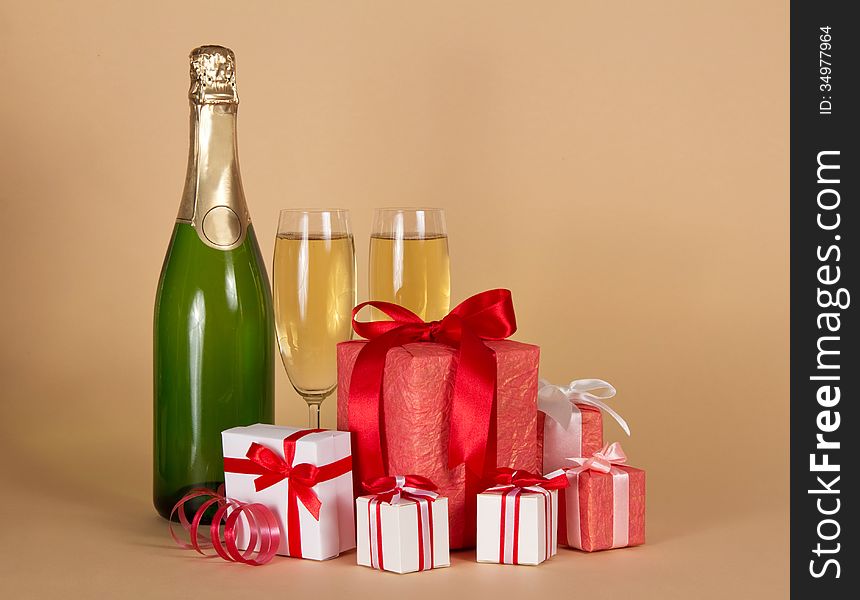 Bottle and wine glasses with champagne, big and small gift boxes on a beige background. Bottle and wine glasses with champagne, big and small gift boxes on a beige background