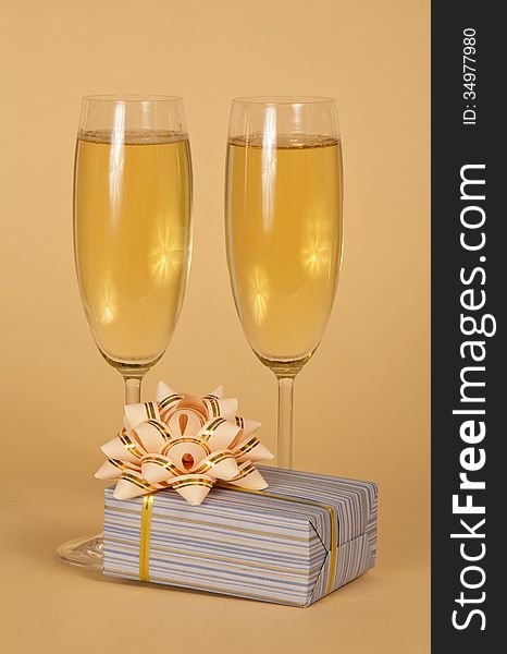 Wine glasses with champagne and a beautiful gift box with a bow on a beige background. Wine glasses with champagne and a beautiful gift box with a bow on a beige background