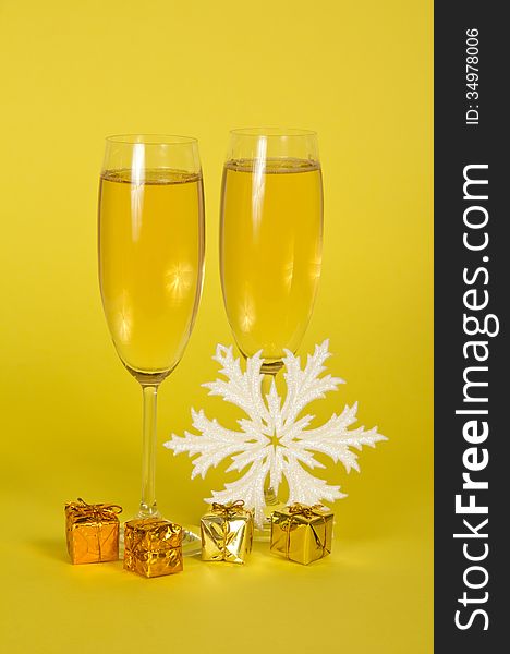 Christmas champagne in wine glasses small gift boxes and a snowflake on a yellow background