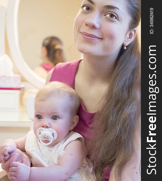 Young mother with the baby of half a year on a lap is siting at a mirror. Young mother with the baby of half a year on a lap is siting at a mirror.