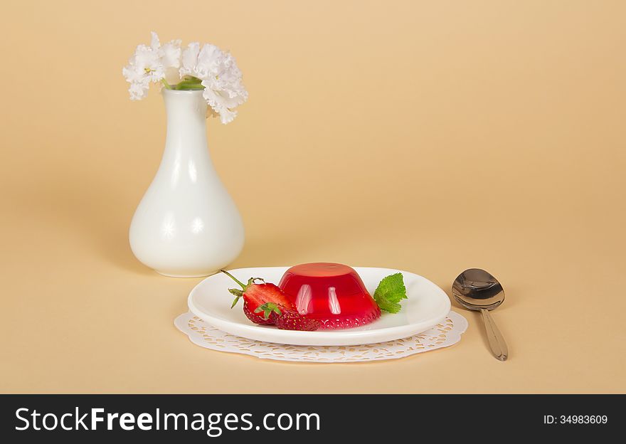 Plate with strawberry jelly, spoon, a napkin and a vase with the flowers on a beige background. Plate with strawberry jelly, spoon, a napkin and a vase with the flowers on a beige background