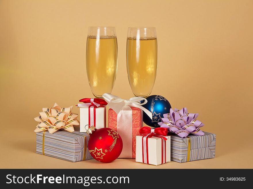 Two wine glasses with champagne, charming gift boxes and Christmas toys on a beige background