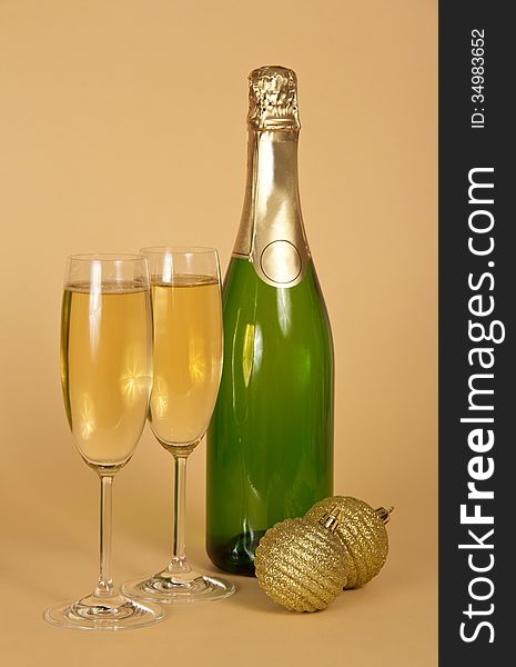 Bottle and two wine glasses with champagne, two golden New Year's balls on a beige background