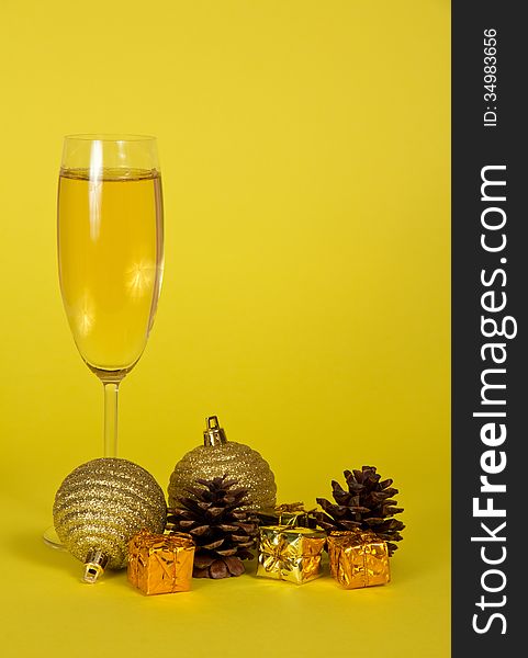 Champagne wine glass, small gift boxes, Christmas toys and pine cones on a yellow background