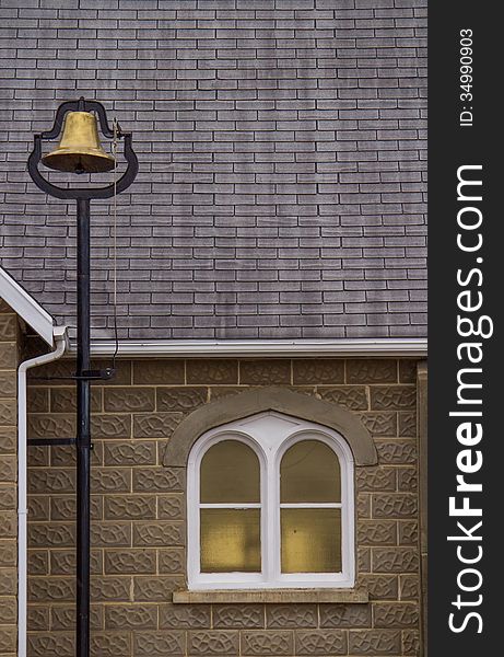 A gold bell beside a white arched church window. A gold bell beside a white arched church window