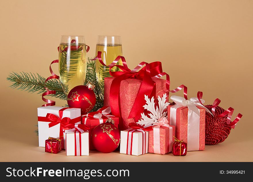 Gift boxes, Christmas toys, serpentine and wine glasses with champagne on a beige background