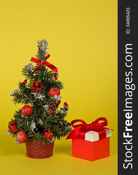 Small fir-tree in a pot with toys and gifts on a yellow background