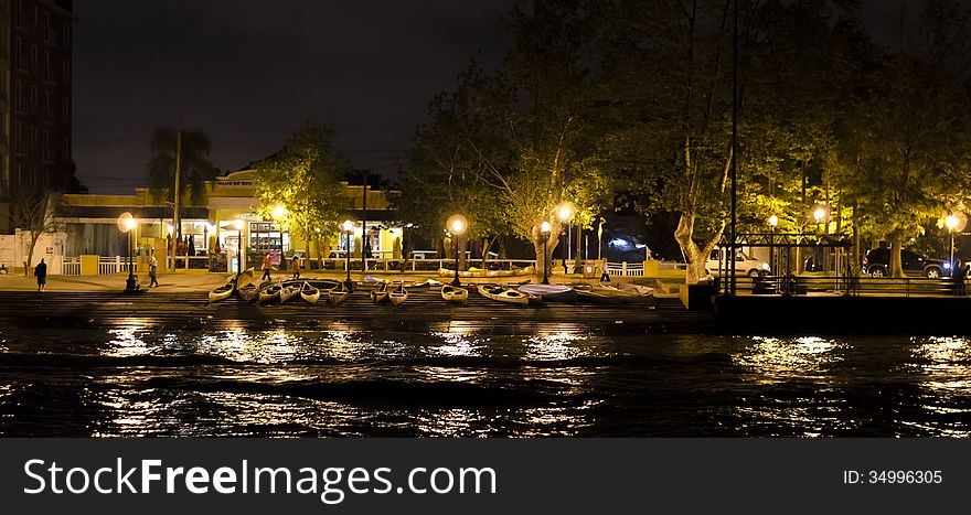 Parked Canoes by canal, along sidewalk lit by lamp posts