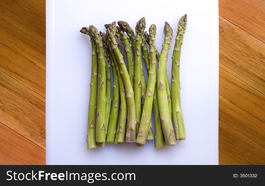 A bunch of fresh green asparagus on a white chopping board to be prepared for cooking