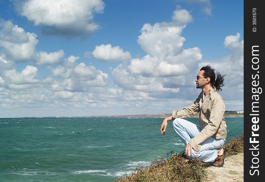 A man over a rock on a blue bay is watching to the horizon. A man over a rock on a blue bay is watching to the horizon