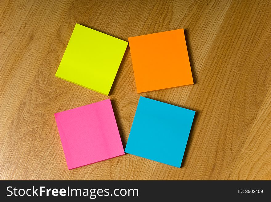Several blank neon colored post-it notes lying on a wooden floor or desk. Several blank neon colored post-it notes lying on a wooden floor or desk