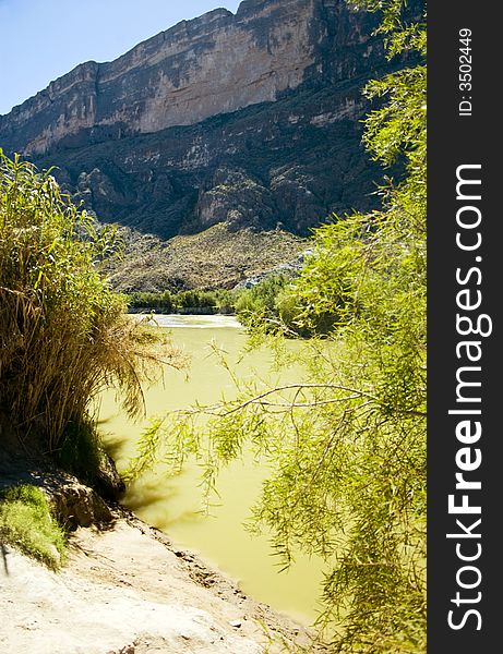 View from the bank of a river with green colored water and high looming cliffs. View from the bank of a river with green colored water and high looming cliffs.