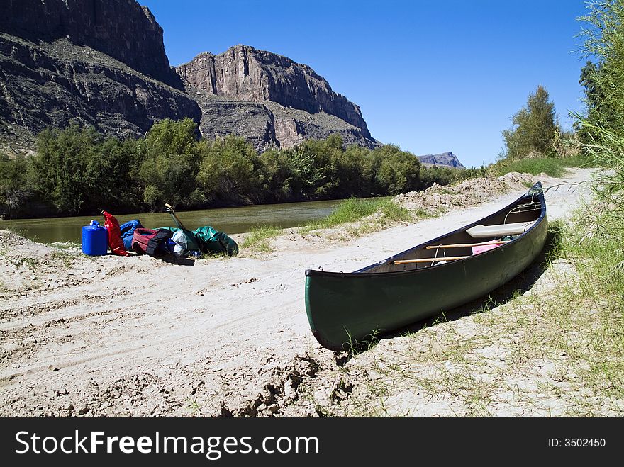 A canoe and gear resting quietly beside a river with majestic cliffs in the background. A canoe and gear resting quietly beside a river with majestic cliffs in the background.