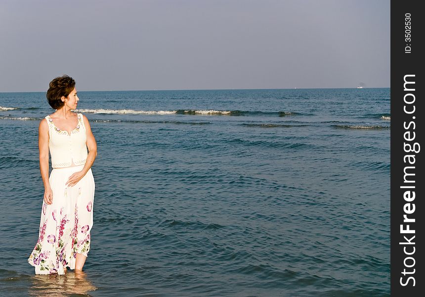 A woman in a long skirt wading in the water along the beach shoreline. A woman in a long skirt wading in the water along the beach shoreline.