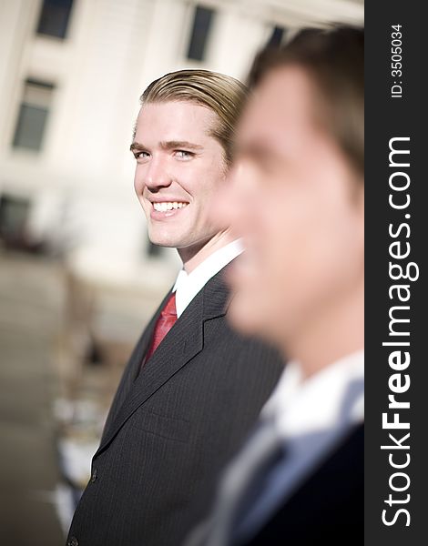 Profile view of two younger businessmen in suits standing with one businessman looking at camera. Profile view of two younger businessmen in suits standing with one businessman looking at camera