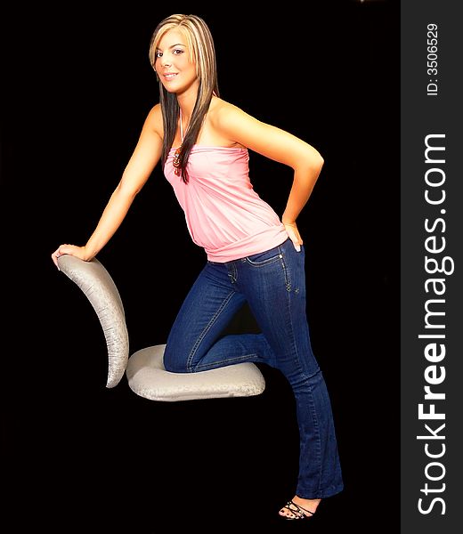 An young lady in jeans and a pink top kneeling on a chair for black 
background. An young lady in jeans and a pink top kneeling on a chair for black 
background.