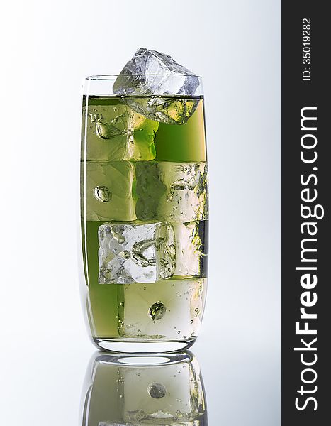 Glass filled with green liquid and ice cubes on a white/grey background (seamless), reflection at the bottom. Glass filled with green liquid and ice cubes on a white/grey background (seamless), reflection at the bottom