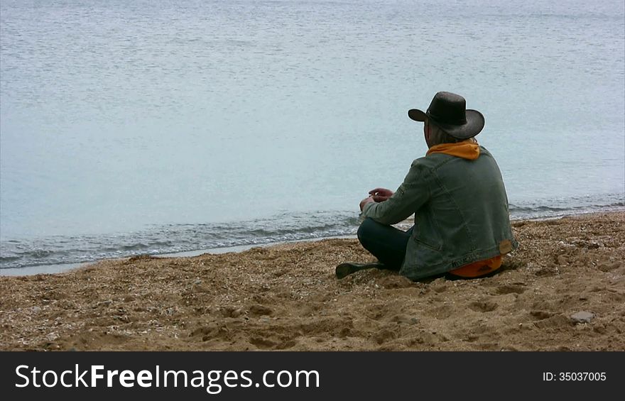Wistful man sits on a sandy beach and threw stones into the water. Wistful man sits on a sandy beach and threw stones into the water