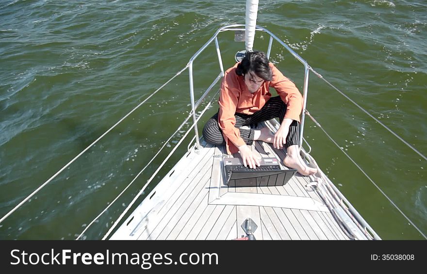 A young man working intently on a laptop on the nose yacht. Yacht racing over the waves in good sunny weather. A young man working intently on a laptop on the nose yacht. Yacht racing over the waves in good sunny weather