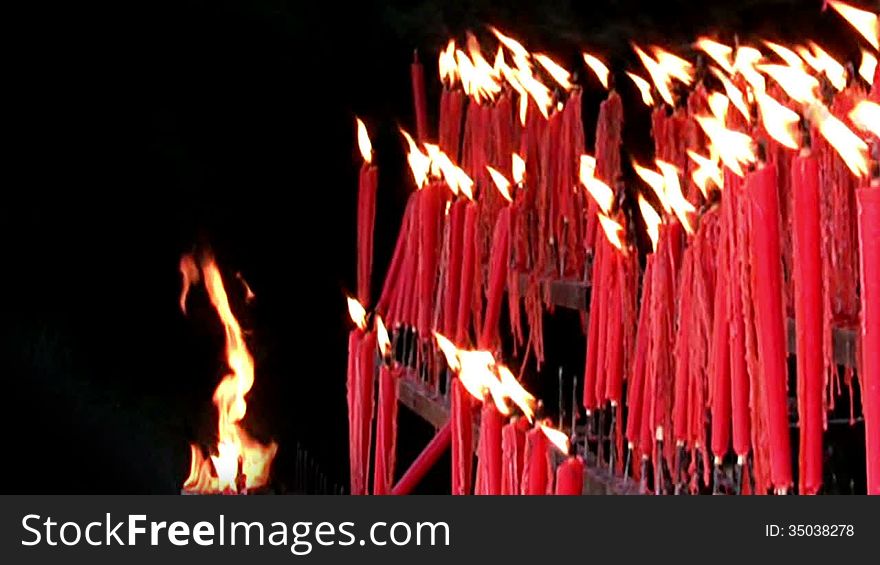 A lot of red ritual candles are burning on a black background. The flames swaying in the wind