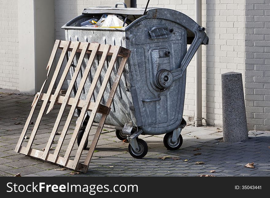 Metal garbage container and a broken pallet. Metal garbage container and a broken pallet