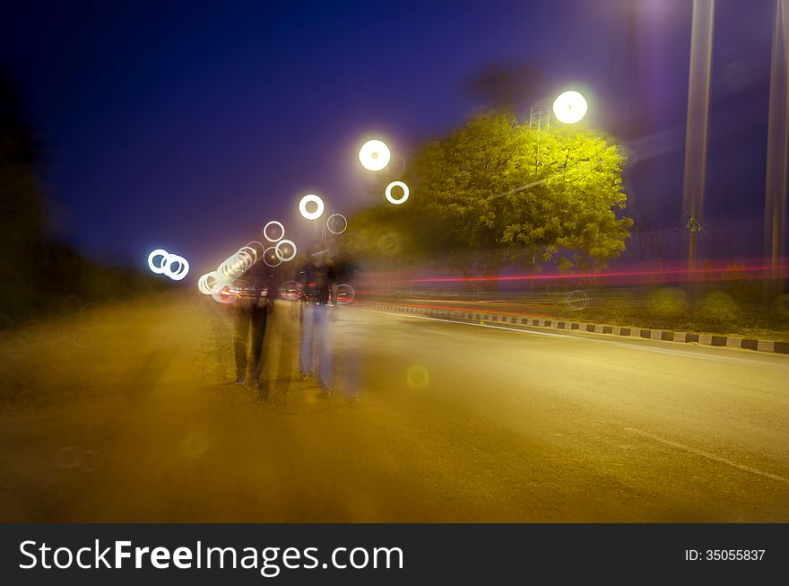 Two persons walking on road with night traffic trails and beautiful colorful bokeh. Two persons walking on road with night traffic trails and beautiful colorful bokeh