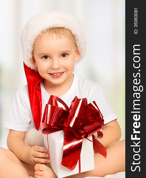 Little cute child boy in a Christmas hat with a gift