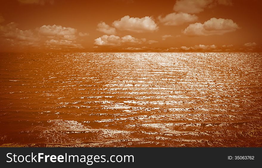 Ripples on the orange sea surface. Orange clouds moving fast on orange sky