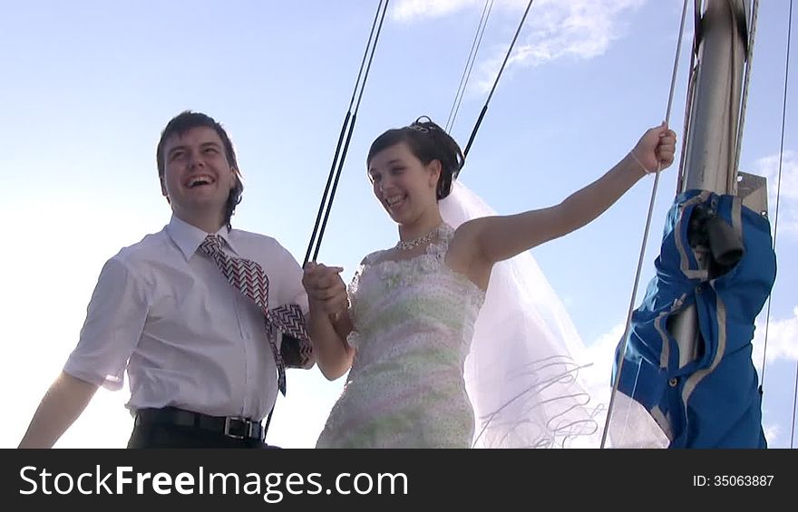 Happy young groom (in white shirt and tie) and his bride (in white wedding dress and veil) on a sailing yacht. Sunset at the cloudless sky the sun caresses with her rays. Happy young groom (in white shirt and tie) and his bride (in white wedding dress and veil) on a sailing yacht. Sunset at the cloudless sky the sun caresses with her rays