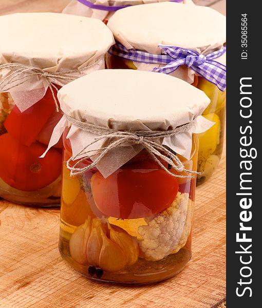 Arrangement of Mixed Pickled Vegetables in Glass Jars Covered with Butter-paper closeup on Wooden background