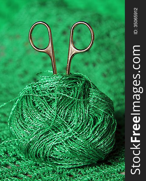 Scissors in a ball of green yarn on a green background