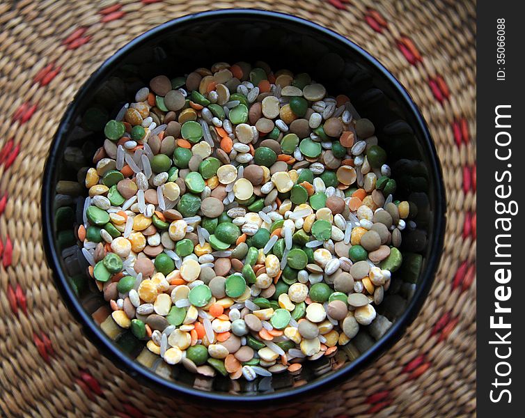 Black plate with a colorful mixture of rice, peas, lentils and barley on a wicker stand. Black plate with a colorful mixture of rice, peas, lentils and barley on a wicker stand